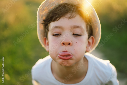 Portrait of a smiling little boy in a white T-shirt and hat playing outdoors on the field at sunset. Happy child, lifestyle. Products for children.