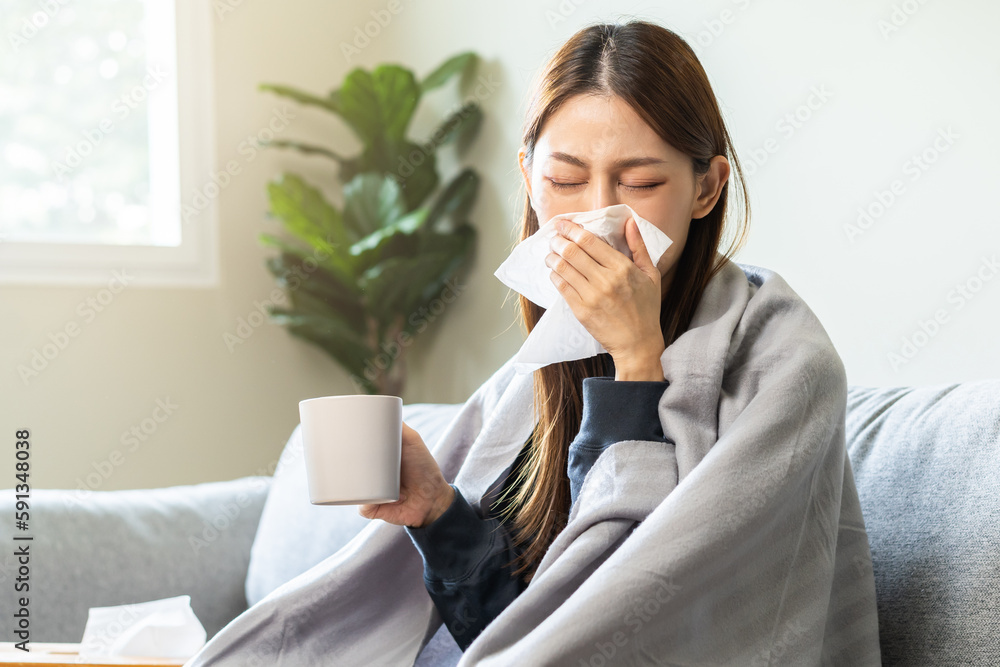 Sick, hurt or pain asian young woman have a fever, flu sore throat, drinking a mug of warm water, use tissues paper sneezing nose, runny while sitting rest on sofa at home. Health care on virus person Sick, hurt or pain asian young woman have a fever, flu sore throat, drinking a mug of warm water, use tissues paper sneezing nose, runny while sitting rest on sofa at home. Health care on virus person