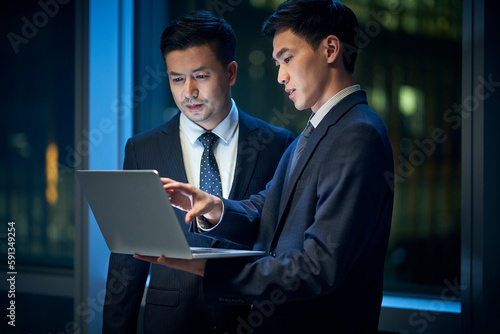 two asian businessmen discussing business in office using laptop computer