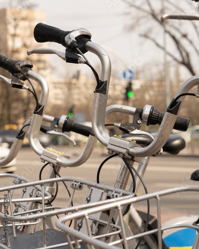 Modern rental electric bikes standing a row during charging on a bright day with a selective focus on the vertical payment terminal with a mock-up of informational or an ad banner placeholder on it