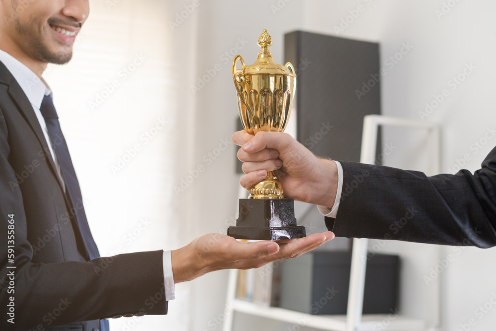 Good job of achievement, happy success asian young businessman, man employee holding golden trophy cup, team getting rewarded for winning from caucasian man boss. Celebration of Teamwork of business. Good job of achievement, happy success asian young businessman, man employee holding golden trophy cup, team getting rewarded for winning from caucasian man boss. Celebration of Teamwork of business.