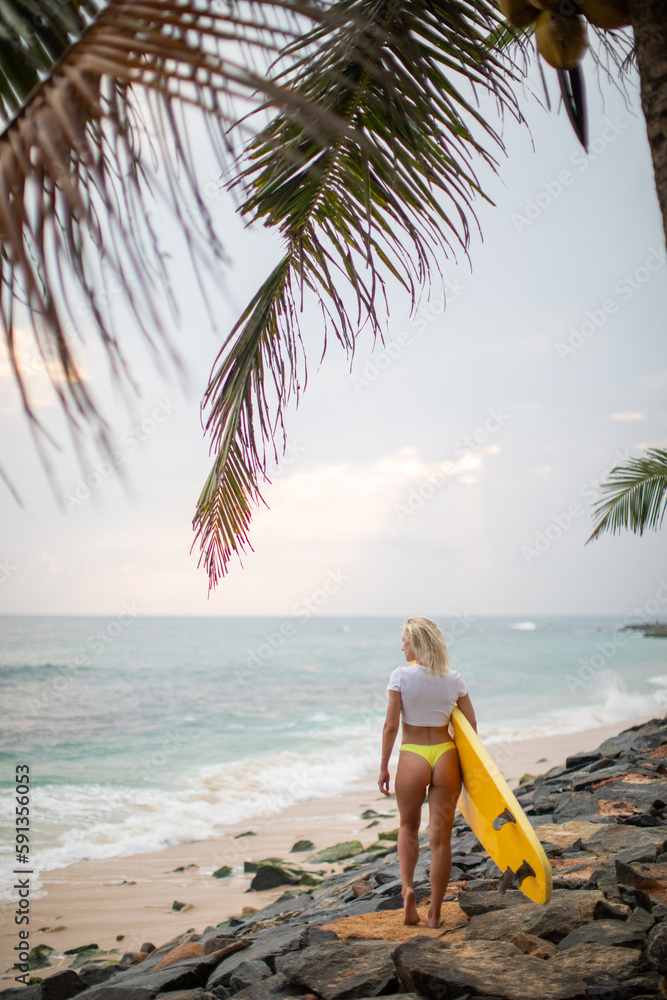 Obraz premium Rear view of a woman in a white cropped t-shirt with a yellow surfboard on the ocean.