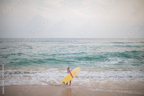 A woman surfer in a pink swimsuit and with a yellow surfboard enters the ocean.