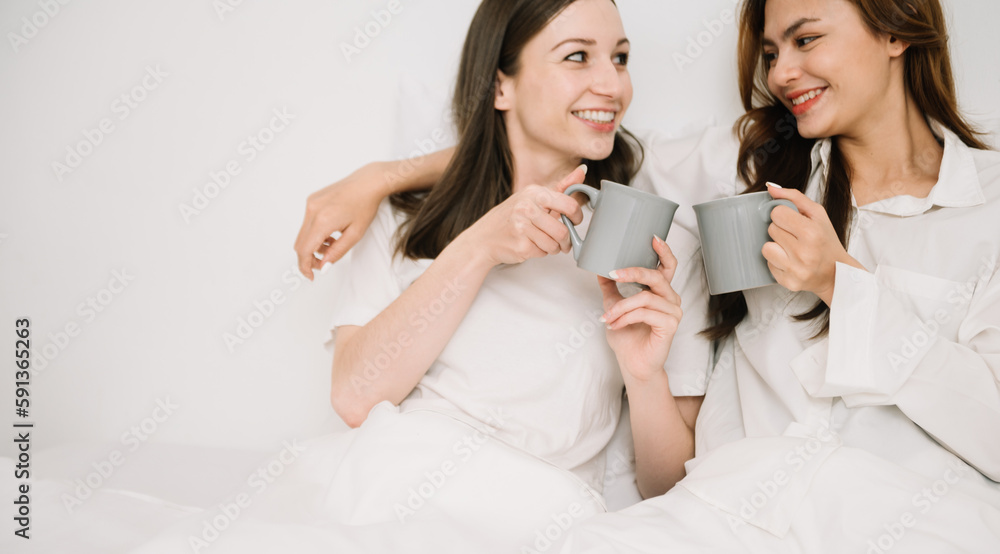 Attractive lesbian couple use mobile phone, tablet watch movie on bed. Beautiful sibling in pajamas lying down with blanket in bedroom together, in morning. Attractive lesbian couple use mobile phone, tablet watch movie on bed. Beautiful sibling in pajamas lying down with blanket in bedroom together, in morning.