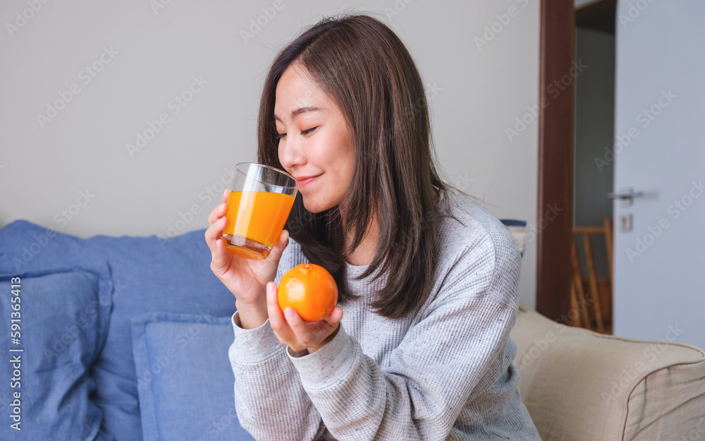 Portrait image of a young woman holding an orange and drinking fresh orange juice at home Portrait image of a young woman holding an orange and drinking fresh orange juice at home