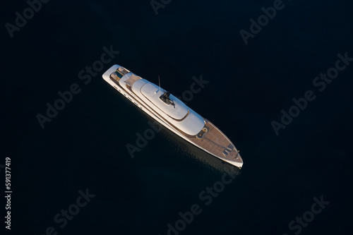 Innovative white big yacht anchored in the morning sun top view. Mega yacht on a dark background aerial view.