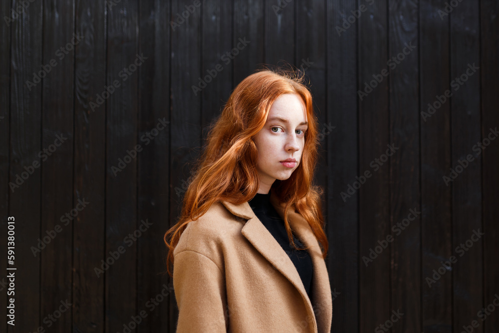 Fototapeta premium young stylish red-haired woman in a coat near her house in autumn