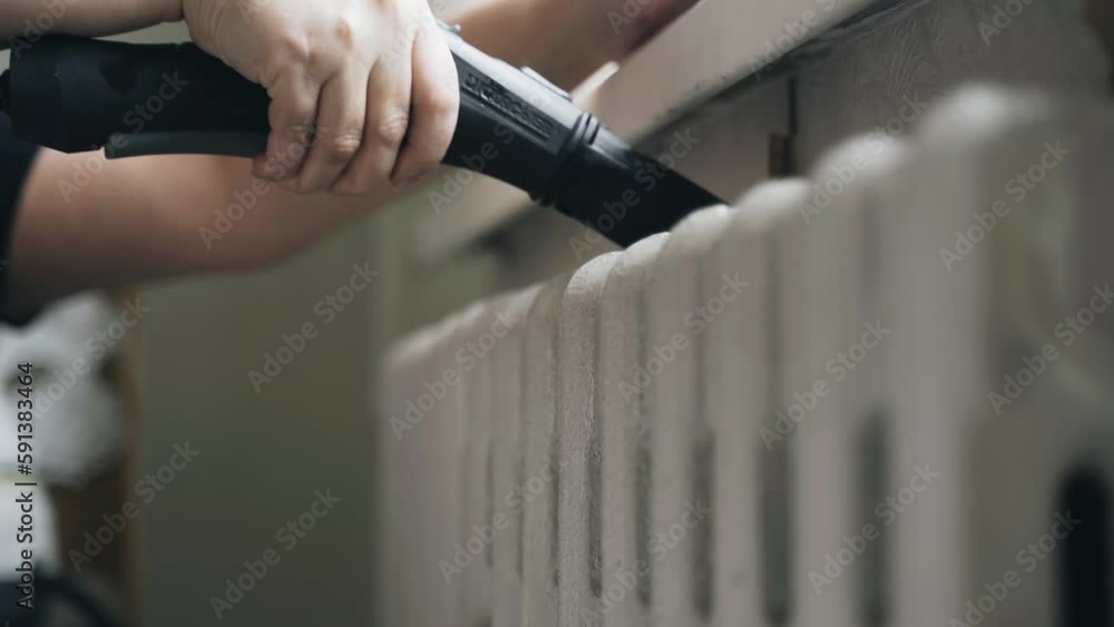 Close-up of female hands cleaning - washing the screen of a heating radiator from dust and dirt using a jet of a steam cleaner. Hygiene and health concept. Close-up of female hands cleaning - washing the screen of a heating radiator from dust and dirt using a jet of a steam cleaner. Hygiene and health concept.