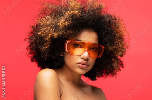 Young woman wearing sunglasses isolated on studio red background. Excited african american female.