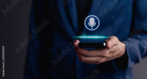 Fotografiet businessman using utilizes his smartphone as an AI assistant, effectively issuing voice commands through its microphone symbol, enhancing productivity with cutting-edge technology