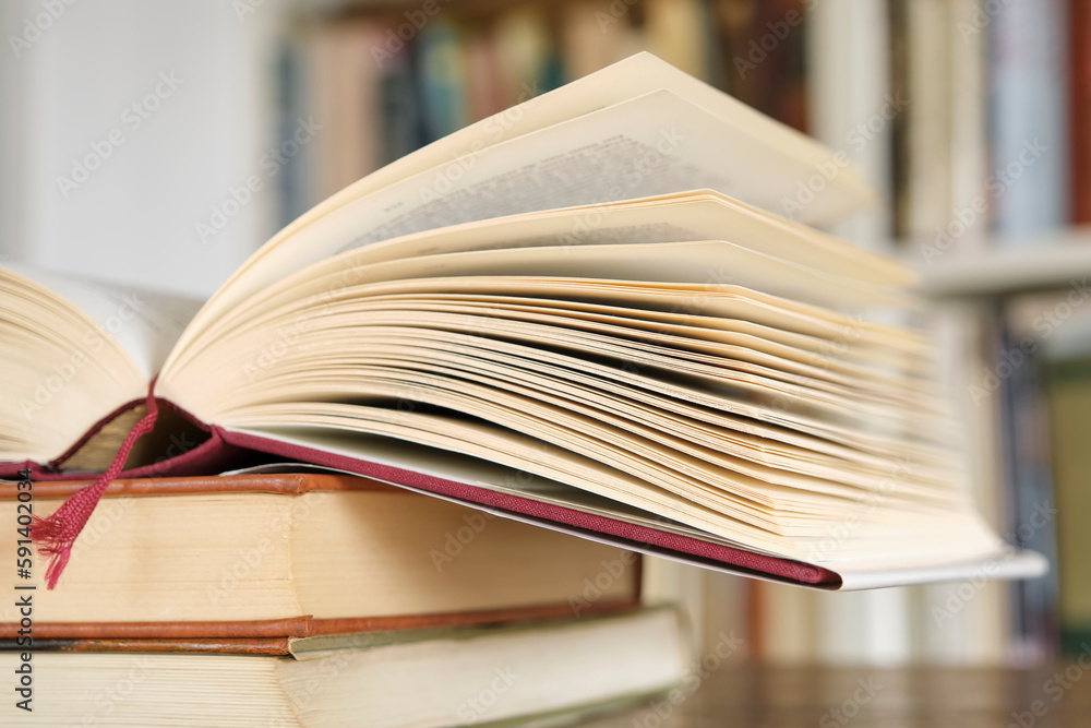 Open book or textbook on a pile of closed books in front of a bookcase