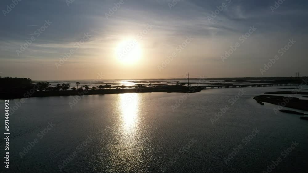 Drone shot of sun setting over salt marsh with cars coming across a bridge, Emerald Isle North Carolina, into the sun, aerial shot Drone shot of sun setting over salt marsh with cars coming across a bridge, Emerald Isle North Carolina, into the sun, aerial shot