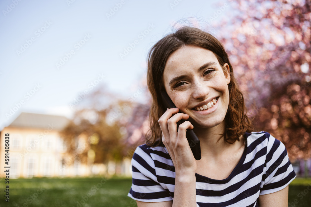 Young woman sitting on a spring meadow in the park and laughing on her phone call Young woman sitting on a spring meadow in the park and laughing on her phone call