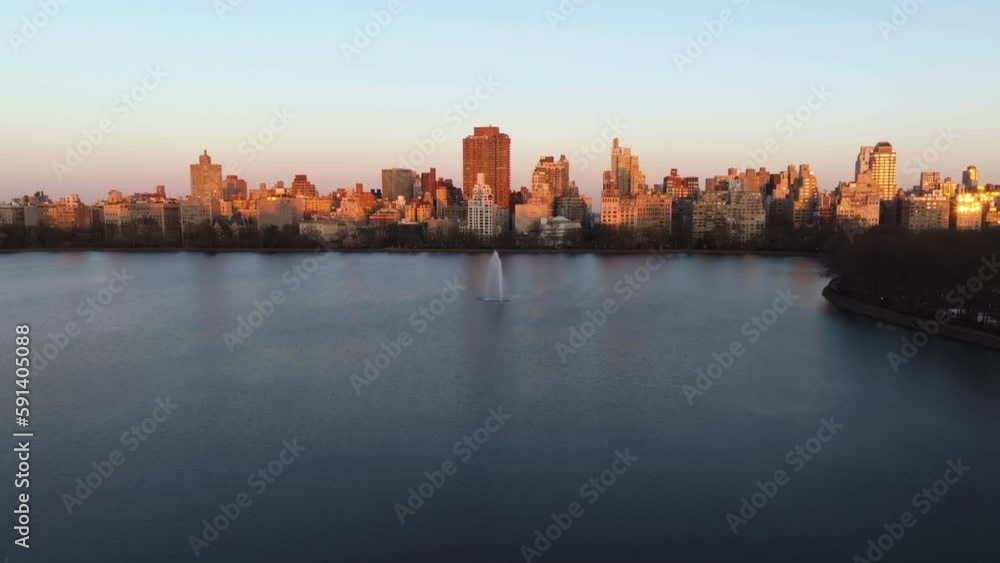Drone shot approaching the Central park reservoir fountain with urban background, dramatic sunset in New York Drone shot approaching the Central park reservoir fountain with urban background, dramatic sunset in New York