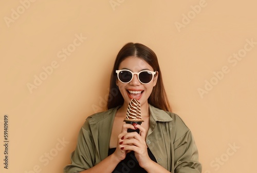 Beautiful young Asian in casual shirt holding big gelato standing over beige background isolated, copy space. Girls Summer joyful concept.