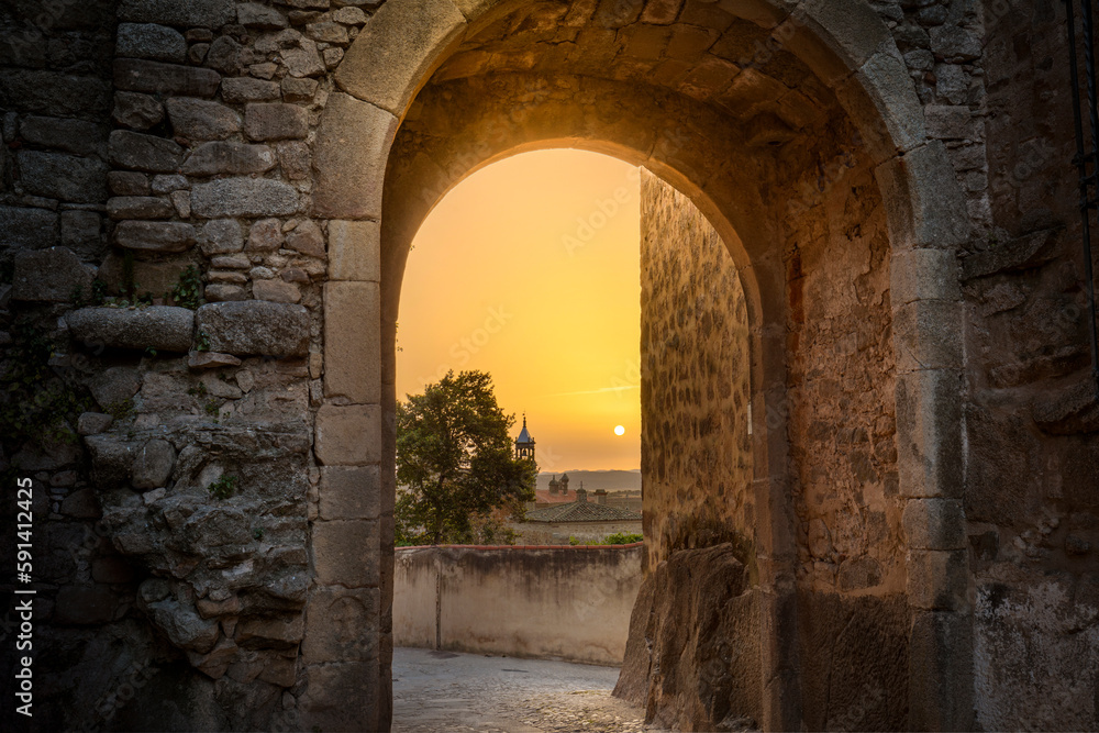 Sun at dawn through the Puerta de Santiago de Trujillo, Cáceres, Spain. Medieval walled stone gate