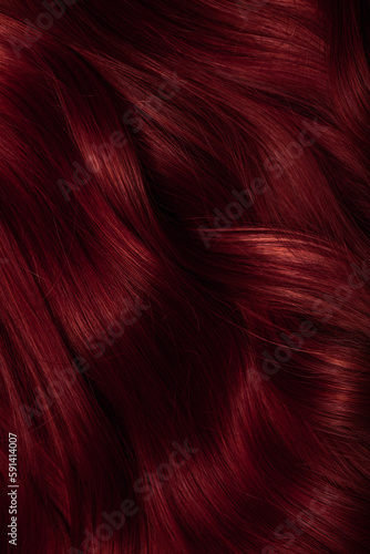 Dark red hair close-up as a background. Women s long brown hair. Beautifully styled wavy shiny curls. Coloring hair with bright shades. Hairdressing procedures  extension.