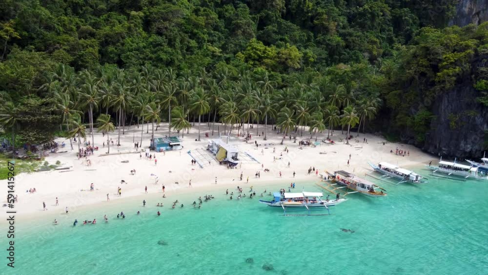 Aerial drone view of Tropical Seven Commandos Beach. Filipino Banca boats unloading tourists for a swim in azure clear water surrounded by palm trees, green limestone mountains in El Nido Philippines Aerial drone view of Tropical Seven Commandos Beach. Filipino Banca boats unloading tourists for a swim in azure clear water surrounded by palm trees, green limestone mountains in El Nido Philippines