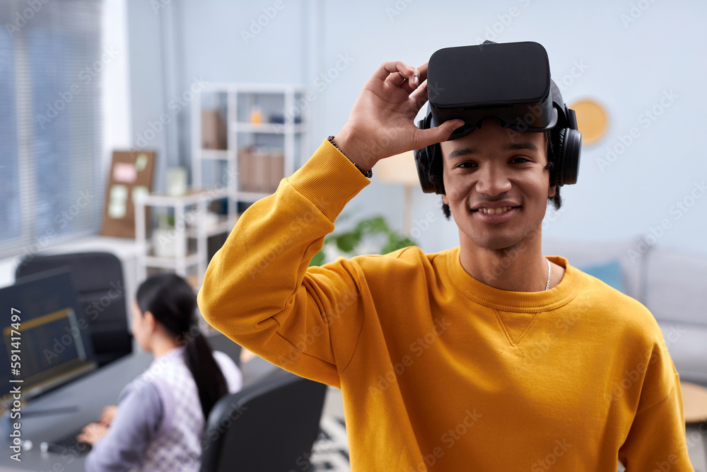 Waist up portrait of black young man using VR in IT development office and smiling at camera, copy space Waist up portrait of black young man using VR in IT development office and smiling at camera, copy space