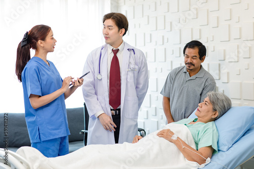 Asian professional successful male doctor in white lab coat with stethoscope female assistant internship nurse in blue uniform holding tablet computer visiting old senior unhealthy patient in ward