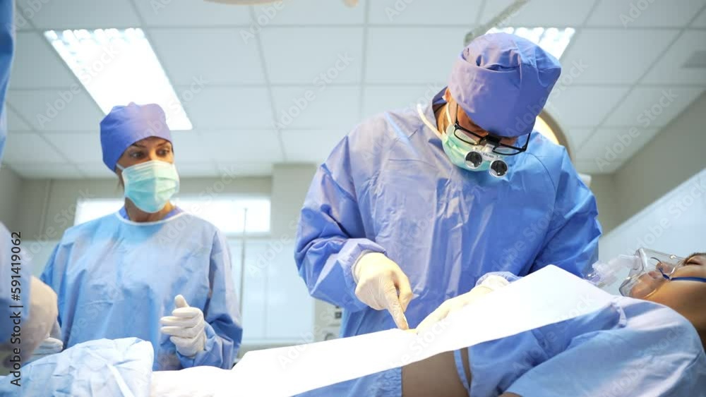 Zoomout and front view of Caucasian male surgeon with his team, in