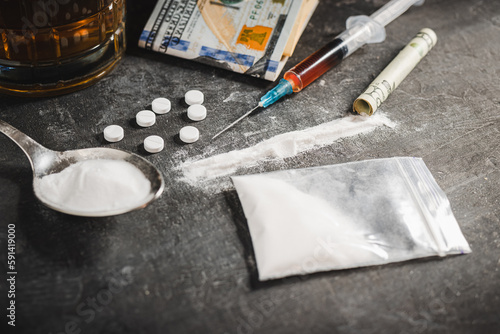 Fotografi Drugs white pill, syringe with a dose of narcotic substances, white powder cocaine, alcohol drink in a glass and US dollar currency on dark background