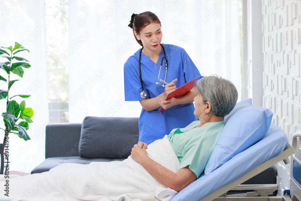 Obraz premium Asian professional successful female internship nurse in blue uniform with stethoscope visiting old senior elderly pensioner woman patient laying lying down on bed writing symptoms down on clipboard