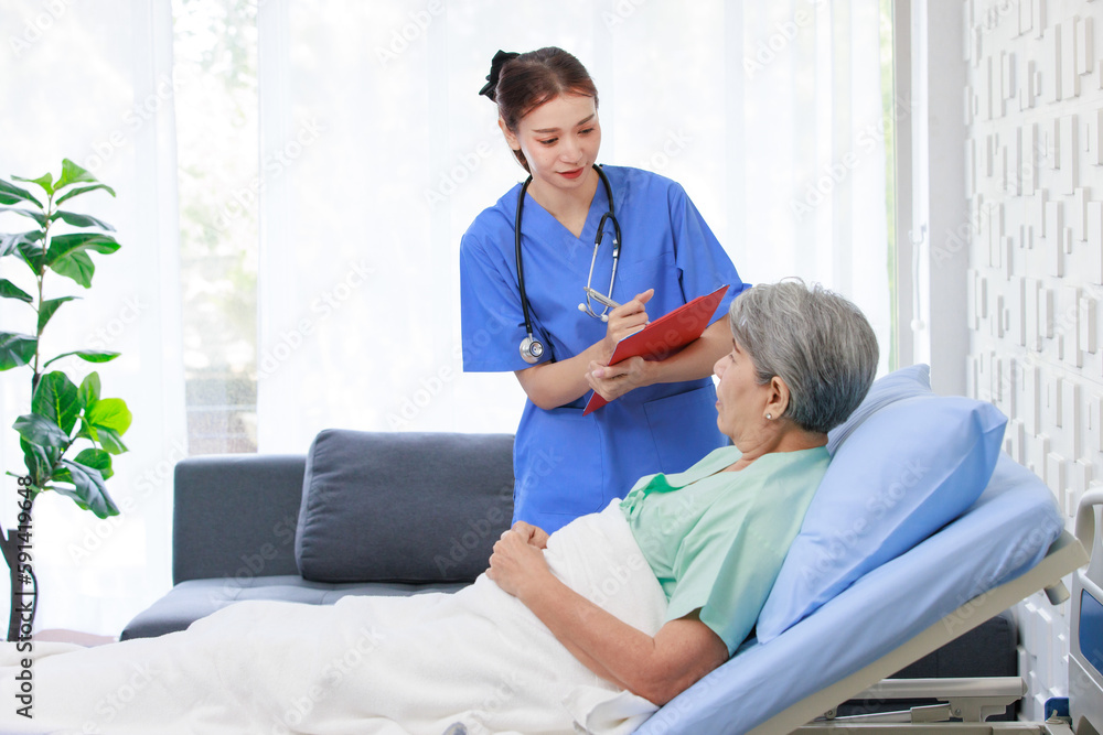 Fototapeta premium Asian professional successful female internship nurse in blue uniform with stethoscope visiting old senior elderly pensioner woman patient laying lying down on bed writing symptoms down on clipboard