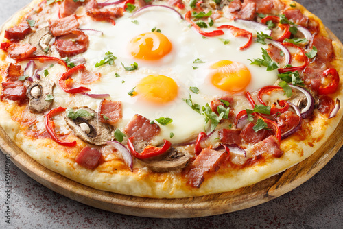 Homemade pizza with bacon, eggs, peppers, mushrooms and red onions close-up on a wooden board on the table. Horizontal