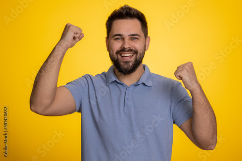 Happy joyful caucasian man shouting, raising fists in gesture I did it, celebrating success, winning, birthday, lottery jackpot goal achievemen, good news. Young adult guy on yellow studio background