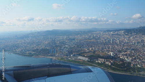 A passenger plane flies over Istanbul, the capital of Turkiye. Houses, streets, roads of Istanbul. Aircraft engine, maneuvers. Flight, travel and tourism. View from a porthole. Sky, clouds, mountains