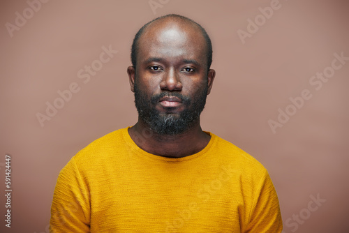 Portrait of African American man with stubble in yellow shirt looking at camera against brown background