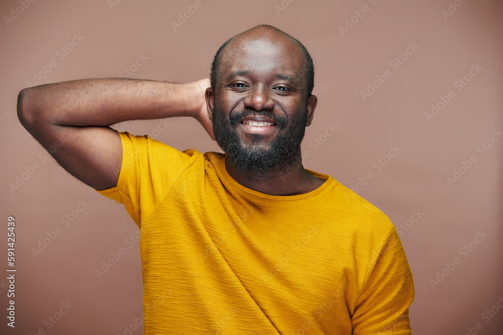 Portrait of positive African American man smiling at camera standing on brown background Portrait of positive African American man smiling at camera standing on brown background