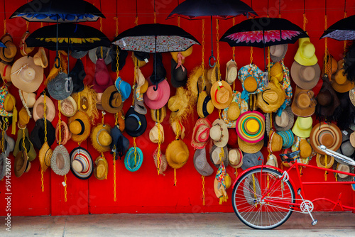 A variety of trendy and colorful hats hang on the red background of a roadside shop. Women's designer sun hats in different colors. Design of women's beach hats. Beach hats for the summer.