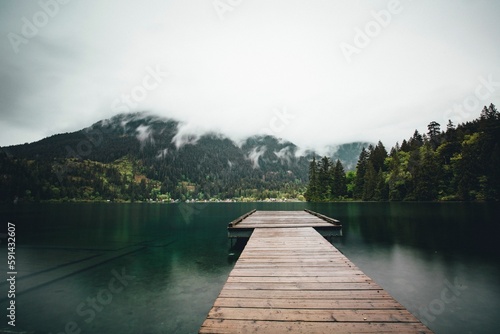 Foto Wooden dock on a lake and a mountain of evergreen trees covered with mist