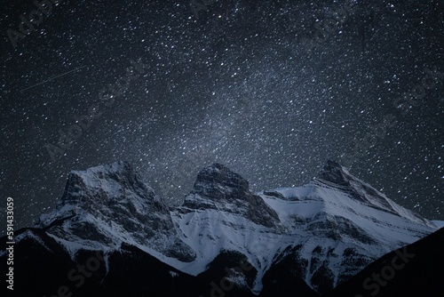 Scenic shot of the sky at night during snowy weather and rocky mountains with white peaks © Rachelmcgrath/Wirestock Creators