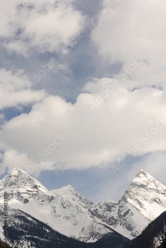 Vertical aerial view of steep snowy mountains under blue cloudy sky