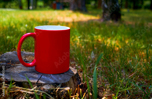 Red cup mug for a drink on a stump in a sunny meadow on a warm sunny day