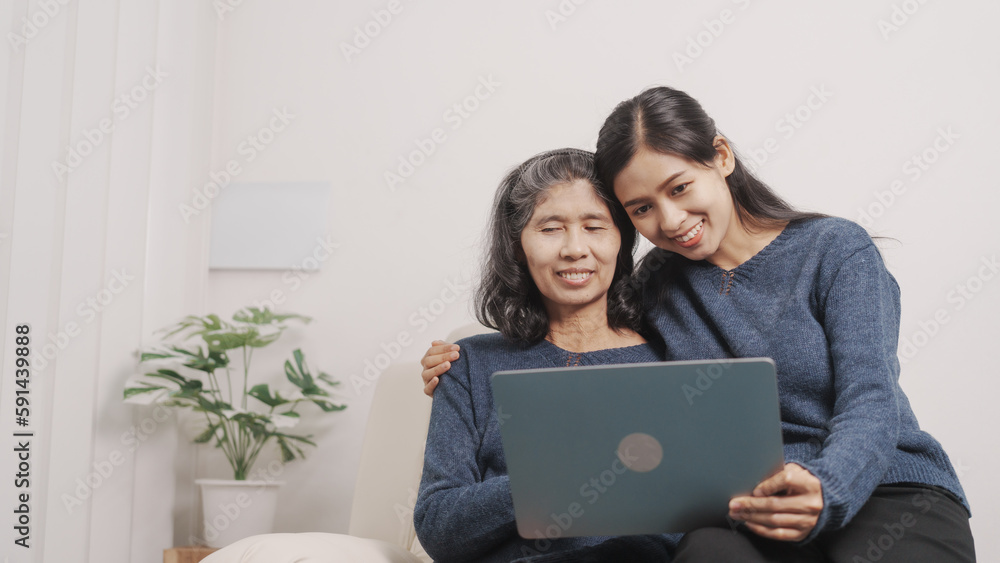 Using laptop, online shopping, Mother's day concept, young adult female daughter congratulate excited asian elderly mother at sofa with birthday anniversary, two generations family photo, real people. Using laptop, online shopping, Mother's day concept, young adult female daughter congratulate excited asian elderly mother at sofa with birthday anniversary, two generations family photo, real people.