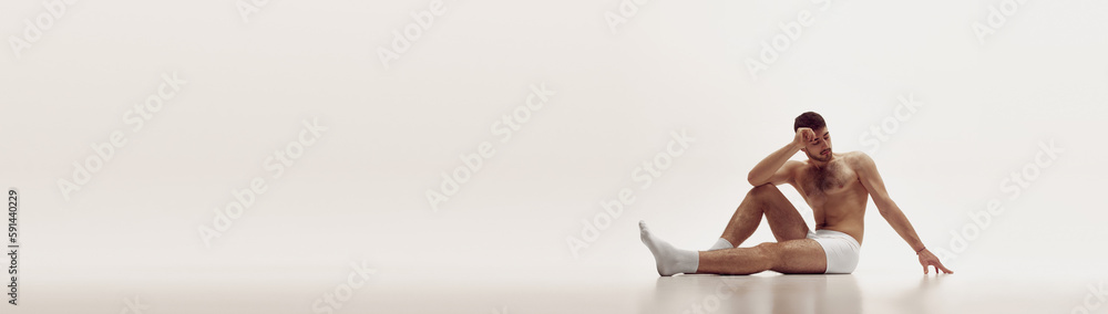 Obraz premium Handsome young muscular man posing shirtless over light studio background. Banner with copy space, text. Aesthetics of male body