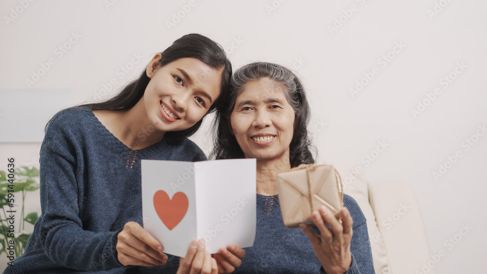 greeting card, Mother's day concept, young adult female daughter congratulate excited asian elderly mother at sofa with birthday anniversary, two generations family photo, real people. greeting card, Mother's day concept, young adult female daughter congratulate excited asian elderly mother at sofa with birthday anniversary, two generations family photo, real people.