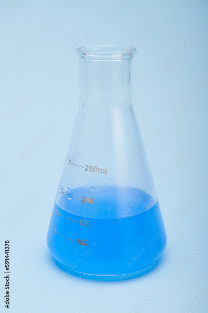 Still life with graduated flat bottomed lab flask with blue liquid solution, isolated over blue color background. Chemistry. Science, Clinical research. Healthcare and medicine concept. Vertical shot Still life with graduated flat bottomed lab flask with blue liquid solution, isolated over blue color background. Chemistry. Science, Clinical research. Healthcare and medicine concept. Vertical shot