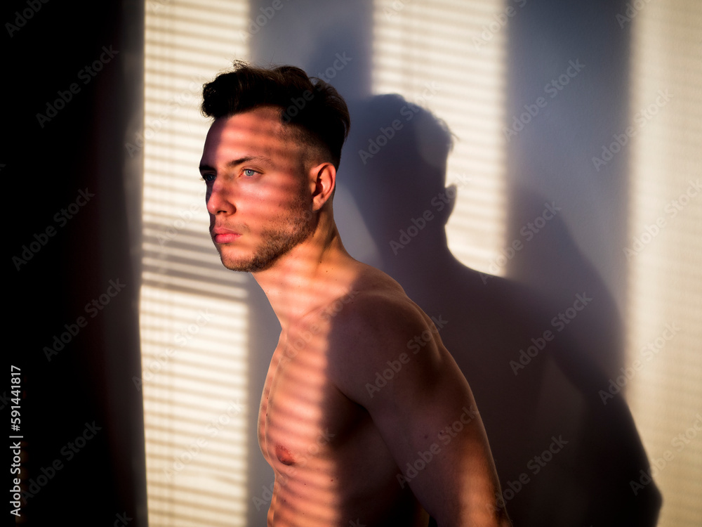 Obraz premium Pensive topless man in shadow stripes from window