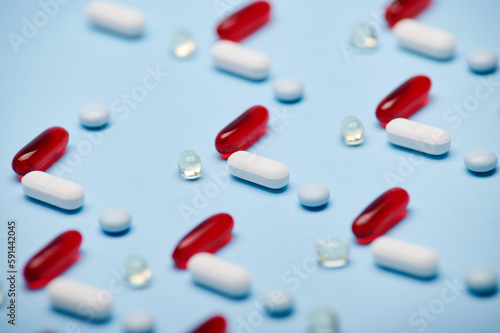 Macro shot medical pills, translucent dragees and gelatin capsules fith fat-solubles vitamins and essential oils, laid out in pattern on isolated blue background. Pharmaceutical industry. Health Day