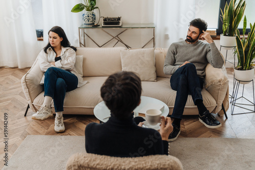 Married couple sitting on opposite sides of couch during therapy session with psychologist