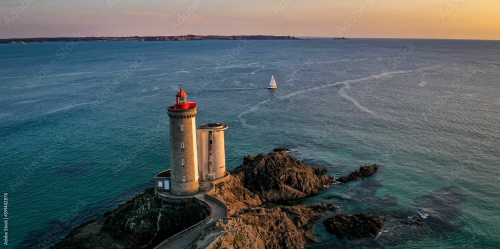 Fototapeta premium Aerial view of a beautiful seascape with a white lighthouse and a sailboat in the background
