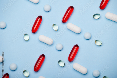 Flat lay. Background of medical pills, red translucent gel capsules and dragee laid out in pattern on isolated blue background. Antidepressant therapy. Painkiller. Pharma business and industry concept