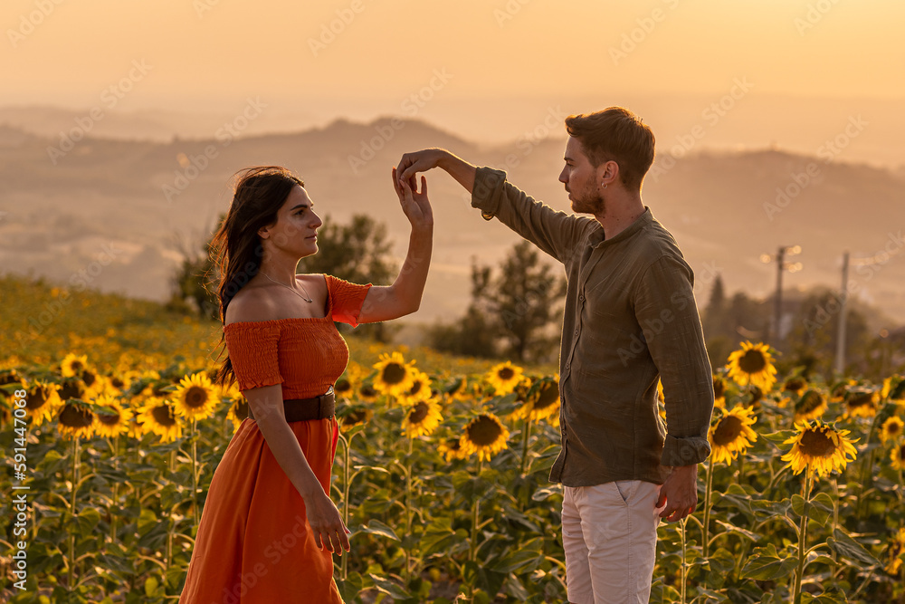 Fototapeta premium Young couple of lovers dancing in a sunflowers field, be my valentine and dnace a tango with me