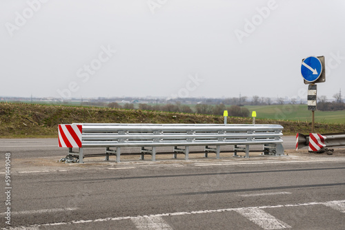 Metal road fencing of barrier type on freeway. Road guard rails. Safety barrier with a red and white striped sign. Installation of median crash barriers on highway. Protect vehicles from accidents.