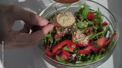 woman's hands skillfully sprinkle food yeast over a vibrant vegetable salad with a wooden spoon, showcasing the nutritional boost. Nutritional Yeast: A Flavorful and Nutrient-Packed Addition
